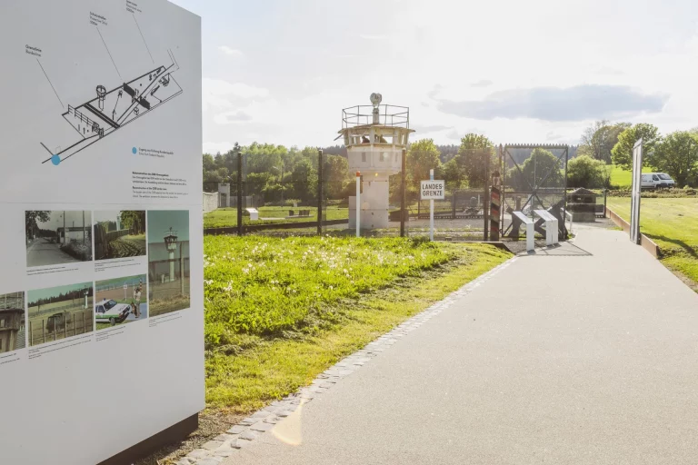 Infotafel zur ehemaligen Grenzanlage neben Wachturm und Grenzzaun am Wegeabschnitt in Mödlareuth