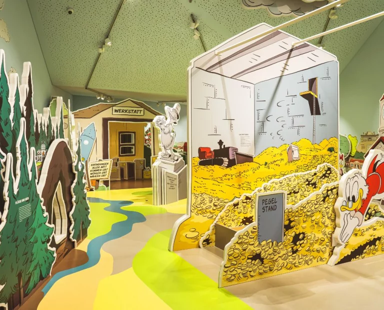 Comicartige Museumsausstellung mit Figuren, Werkstatt-Kulisse und Geldspeicher-Nachbau