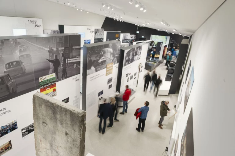 Ausstellungsraum im Deutsch-Deutschen Museum Mödlareuth mit Mauerrest und Besuchergruppen an Infotafeln