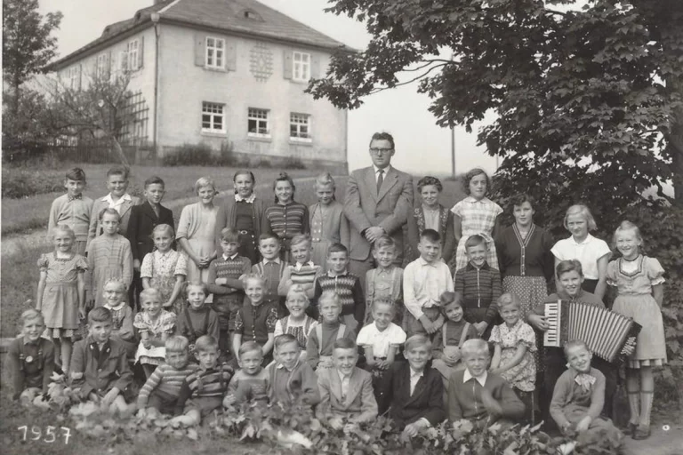 Schwarz-weißes Gruppenfoto einer Schulklasse mit Lehrer vor einem Gebäude, Aufnahme von 1957
