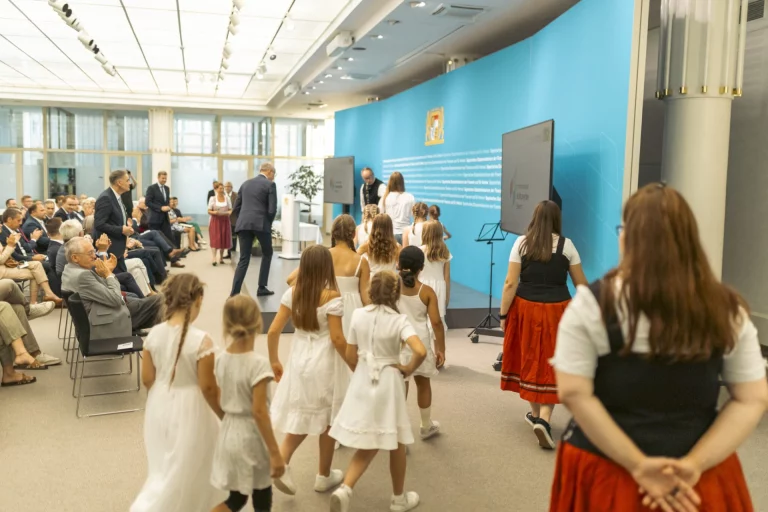 Kinder in weißer Kleidung und Trachtenträgerinnen bei einem Festakt im Foyer