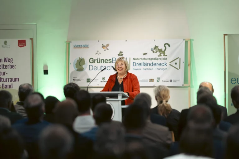 Frau am Rednerpult bei der Eröffnung vor Banner „Naturschutzgroßprojekt Dreiländereck“ und Publikum