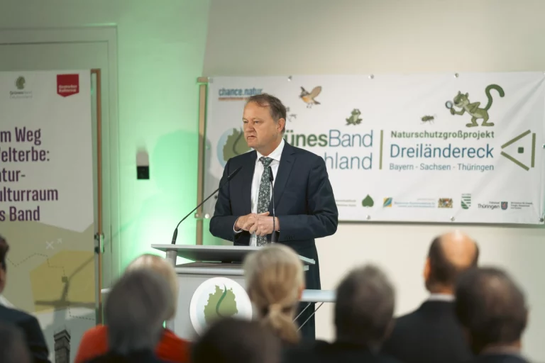 Mann hält Rede am Rednerpult vor Bannern zum Naturschutzgroßprojekt Grünes Band Dreiländereck