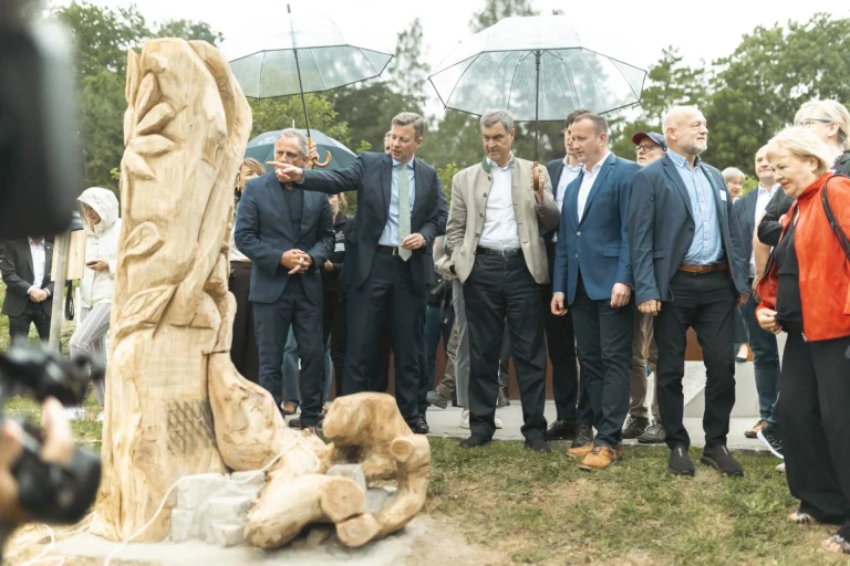 Männer in Jacken betrachten eine Holzskulptur im Grünen Band bei Mödlareuth