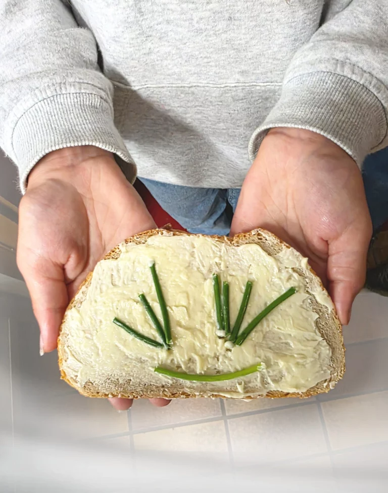 Kinderhände halten Butterbrot mit Schnittlauch-Gesicht