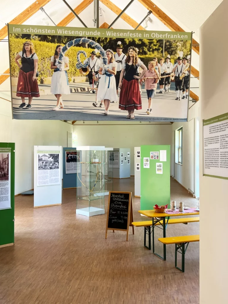 Museumsraum mit Ausstellungsbanner zu Wiesenfesten in Oberfranken sowie Vitrinen, Infotafeln und Bierzeltgarnitur
