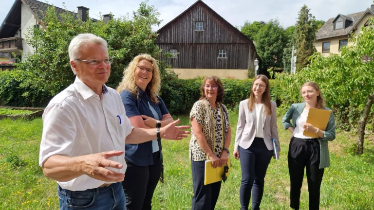 Mann im Gespräch mit vier Frauen auf einer Grünfläche vor historischem Scheunengebäude