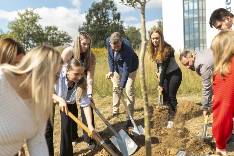 Gruppe von Personen pflanzt gemeinsam einen Baum vor dem Landratsamt