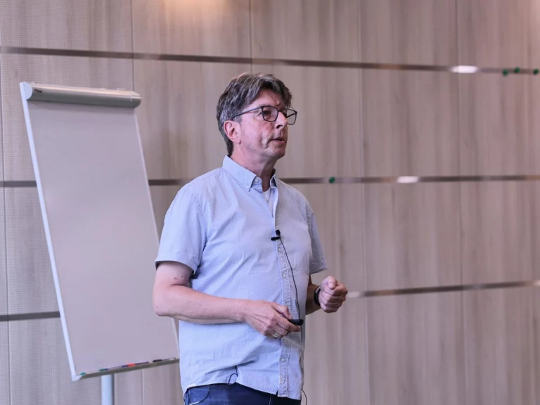 Mann in Freizeithemd spricht vor einem Flipchart bei einer Veranstaltung