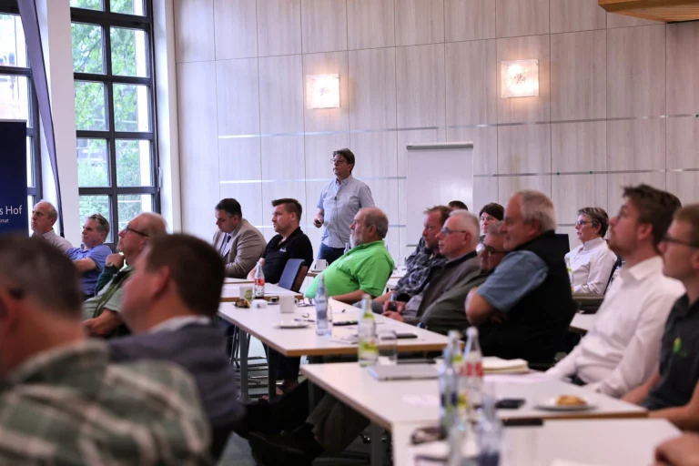Teilnehmer im Seminarraum verfolgen Vortrag eines stehenden Referenten beim Waldsymposium