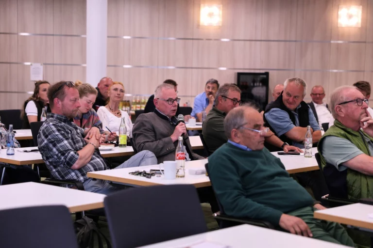 Teilnehmer an Tischen im Sitzungssaal, einer spricht mit Mikrofon beim Waldsymposium