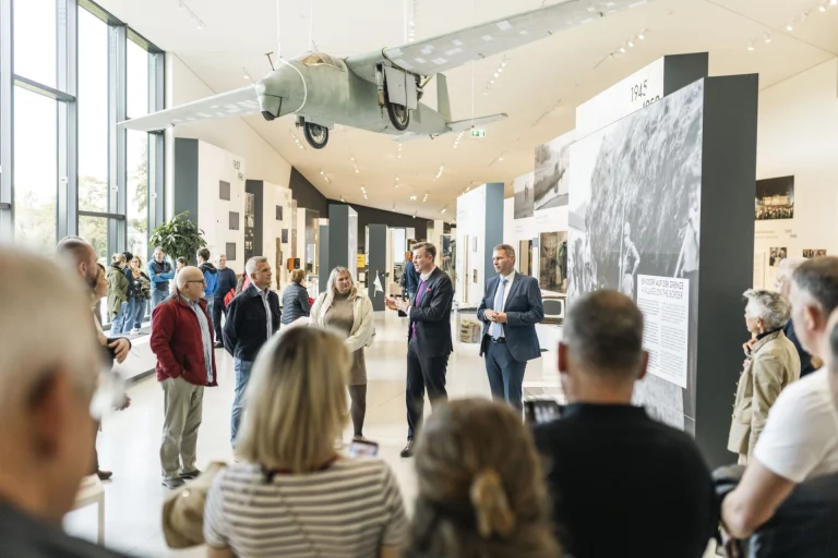 Gruppe von Personen in einer Museumsausstellung, zwei Männer im Gespräch vor Informationstafeln