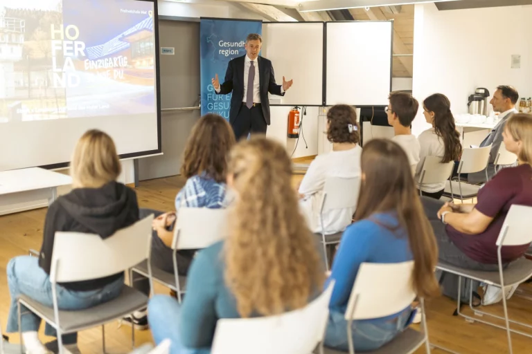 Mann am Flipchart spricht vor sitzender Gruppe junger Erwachsener im Workshop