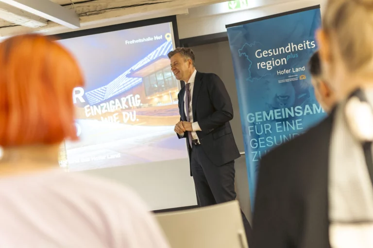 Referent spricht vor Publikum, im Hintergrund Präsentation und Banner der Gesundheitsregion Hofer Land