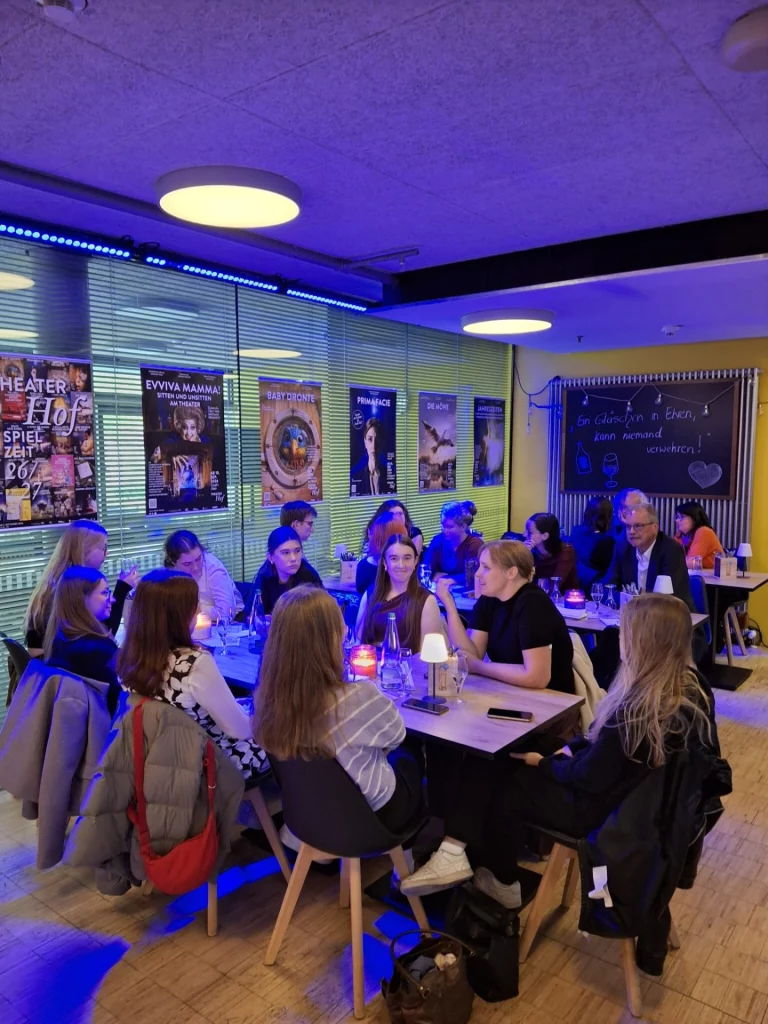 Studierende sitzen in Gruppen an Tischen in einer Veranstaltungslocation und unterhalten sich