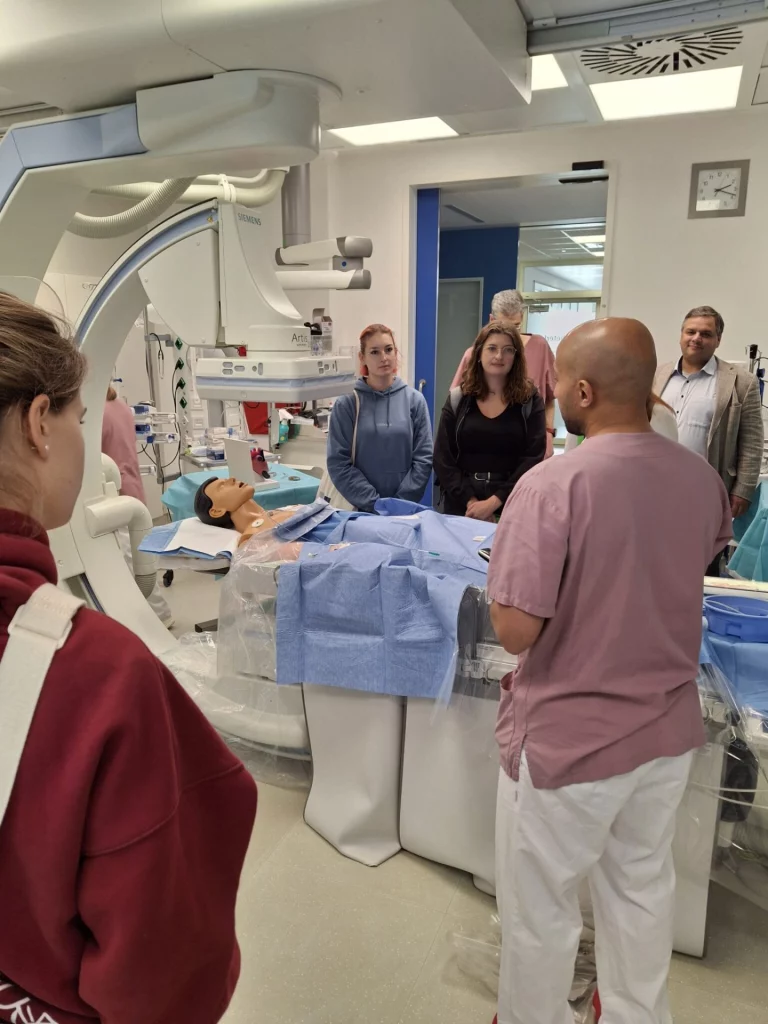 Medizinstudierende und Arzt in OP-Kleidung an Angiographiegerät mit Übungspuppe