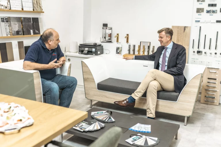 Handwerker und Landrat im Gespräch auf einer Sitzecke im Ausstellungsraum eines Haustechnikbetriebs