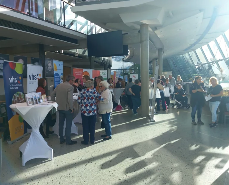 Infostände und Gespräche zwischen Besucherinnen und Besuchern in einem Foyer