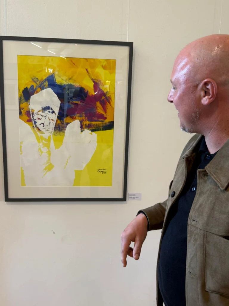 Mann betrachtet gerahmtes Kunstwerk mit Porträt auf gelbem Hintergrund in Ausstellung
