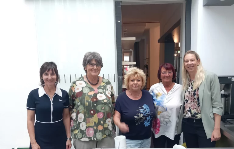 Fünf Frauen stehen gruppiert und lächelnd vor einem Eingangsbereich zusammen